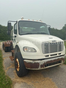 Cab and chassis truck showing Freightliner M2 106 front grille, white cab, rusted bumper, and dual mirrors.