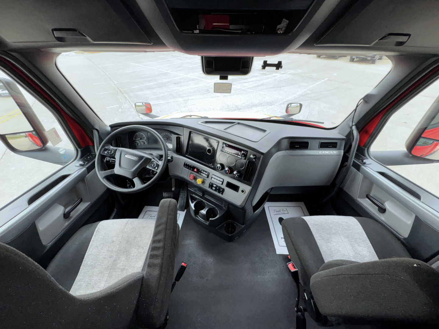 Truck cab interior of a 2023 Freightliner Cascadia 126 with front seats, steering wheel, dashboard, and center console visible.