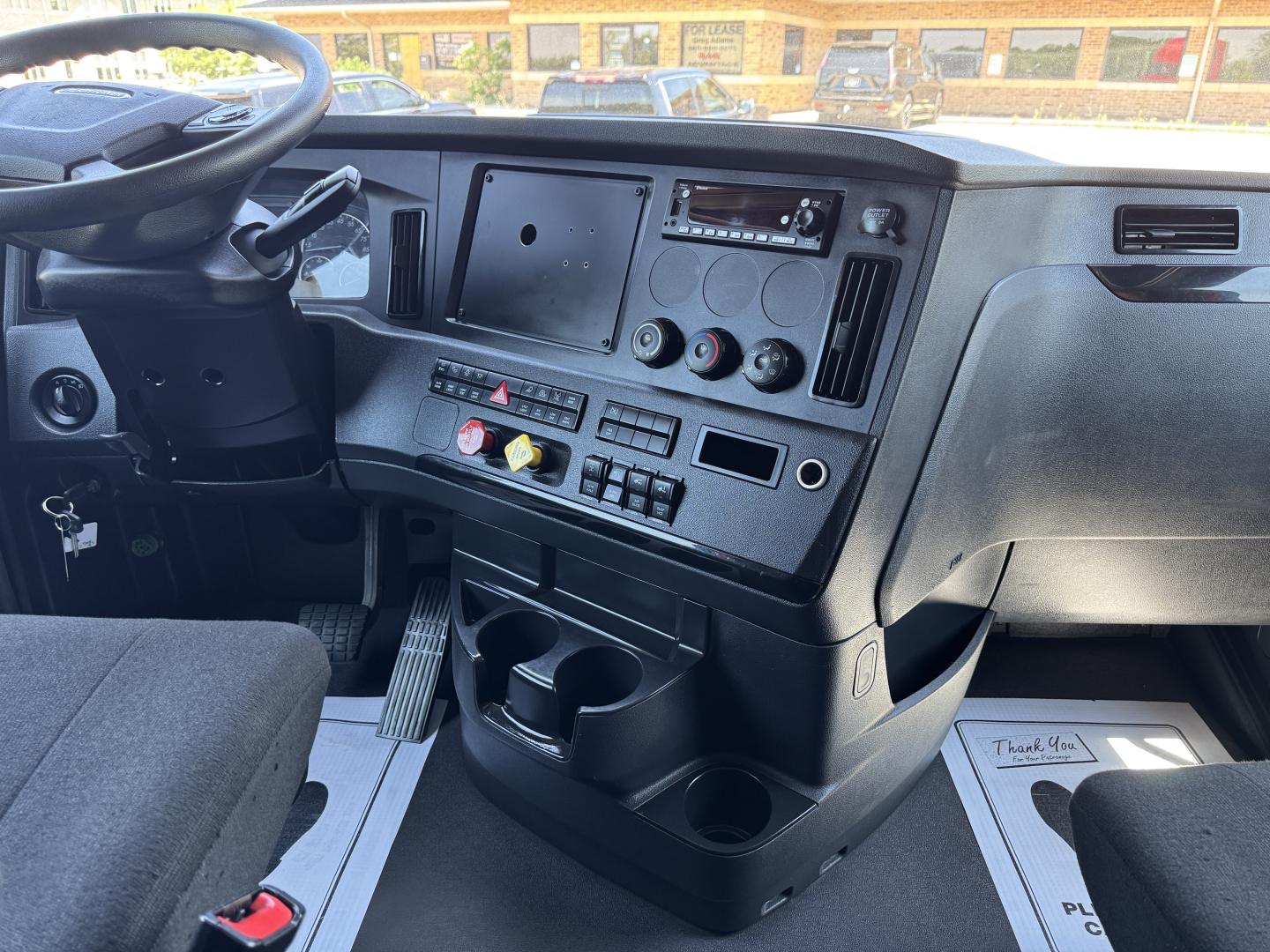 Cab interior of a 2023 Freightliner Cascadia 126 showing steering wheel, dashboard with multiple switches, cup holders, and storage compartments.