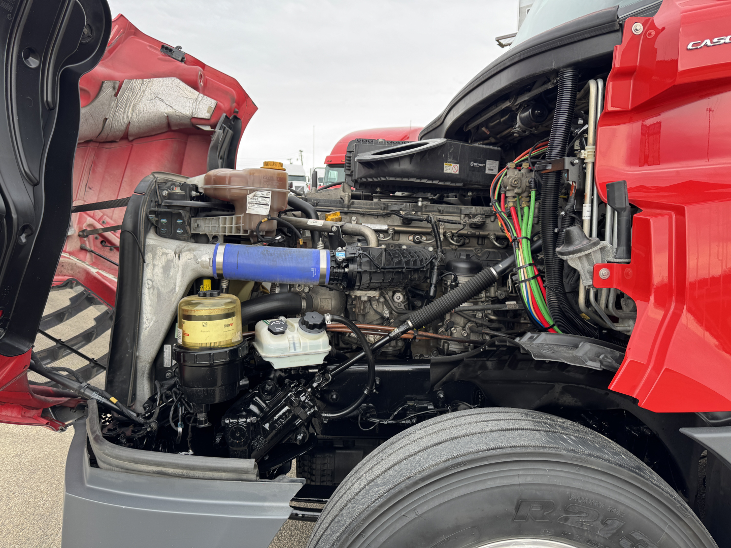 Freightliner Cascadia engine bay showing diesel engine with exposed components, hoses, and wiring.