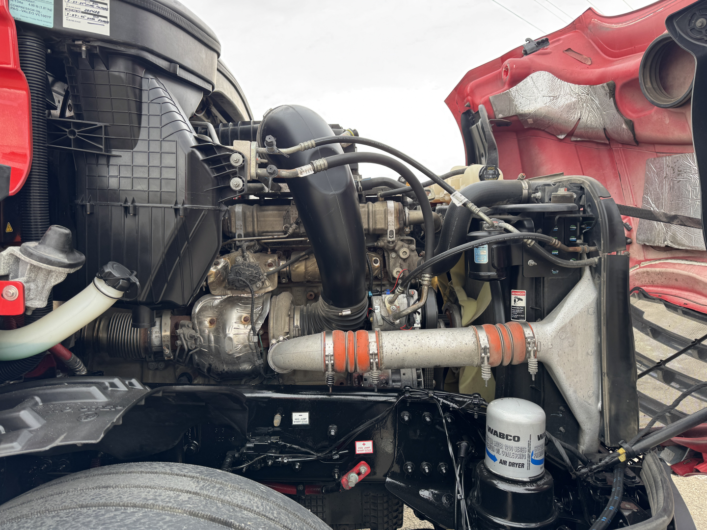 Truck engine bay of a 2023 Freightliner Cascadia 126 with visible diesel engine, air intake, hoses, and coolant reservoir.