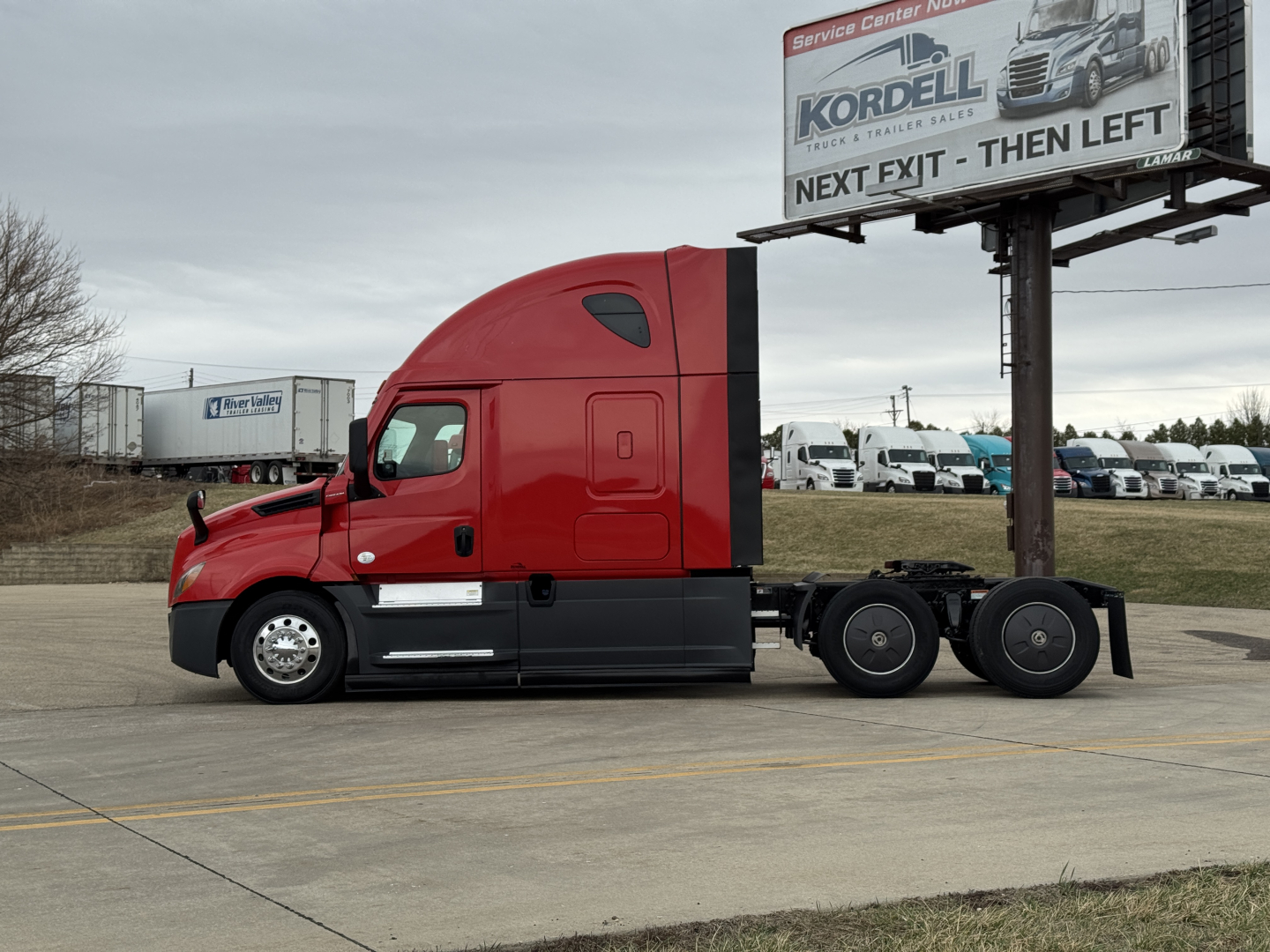 Freightliner Cascadia 126 tractor in red with sleeper cab and dual rear axles, side view on highway with a Kordell sign in background.
