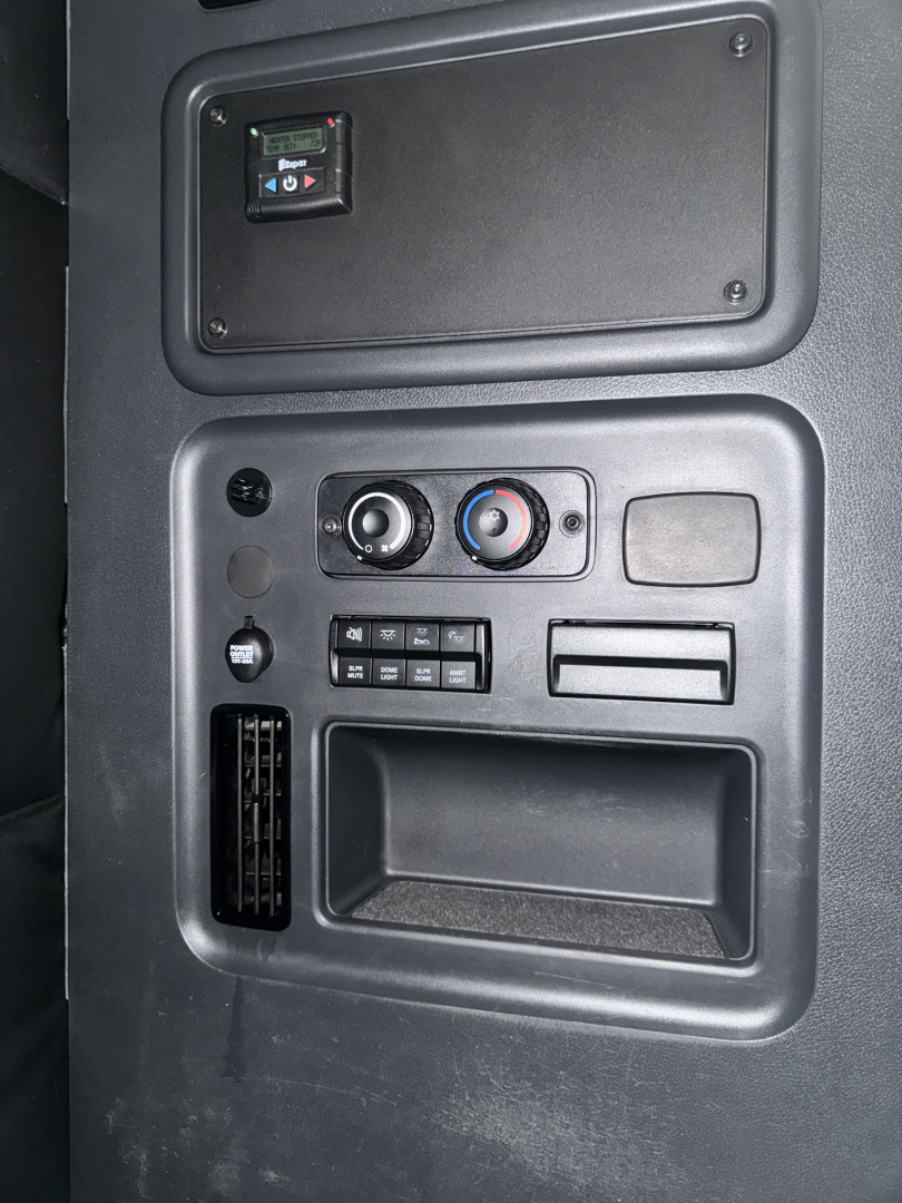 Truck cab panel with controls: climate dials, toggle switch panel, small storage, and vertical vent; part of Freightliner Cascadia interior.