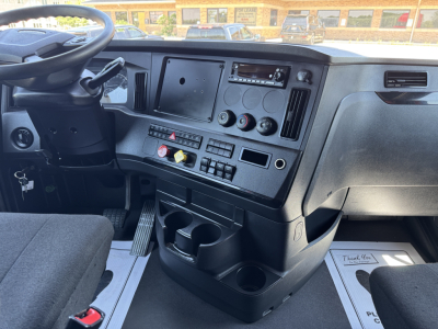 Cab interior of a 2023 Freightliner Cascadia 126 showing steering wheel, dashboard with multiple switches, cup holders, and storage compartments.