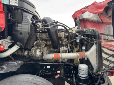 Truck engine bay of a 2023 Freightliner Cascadia 126 with visible diesel engine, air intake, hoses, and coolant reservoir.