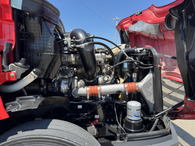 Truck engine bay of a Freightliner Cascadia 126 showing radiator, hoses, air intake, coolant reservoir, and various engine components.