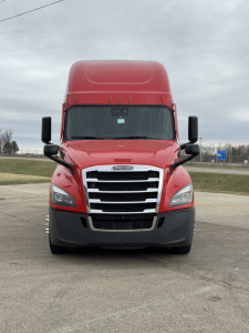 Front view of a red 2023 Freightliner Cascadia 126 truck, showing the grille, headlights, large black bumper, and side mirrors.