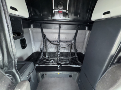 Freightliner Cascadia 126 sleeper cab interior cargo area with netting and storage, view from rear bed area.