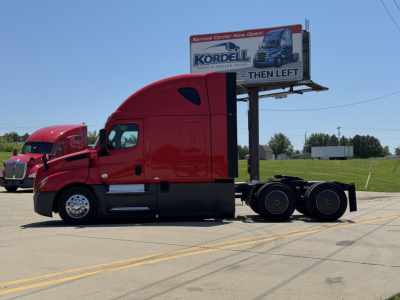 Freightliner Cascadia 126 tractor in red, side view with a billboard in the background.