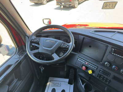 Freightliner Cascadia truck cabin interior showing steering wheel, dashboard with large touchscreen display, and control panel.