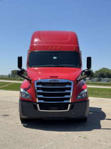 Front view of a red Freightliner Cascadia 126 truck with black bumper and grille, large side mirrors, clear windshield, blue sky.