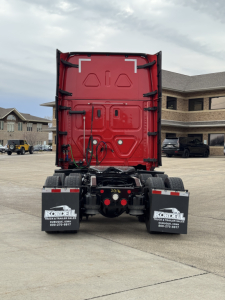Rear view of a red Freightliner Cascadia truck cab with black mudflaps and white Kordell plates, showing the back doors and chassis.