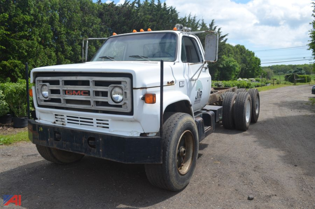 GMC TopKick C70 cab and chassis truck showing front grille with GMC badge and dual headlights, single cab, dual rear wheels, light-colored body with service decal