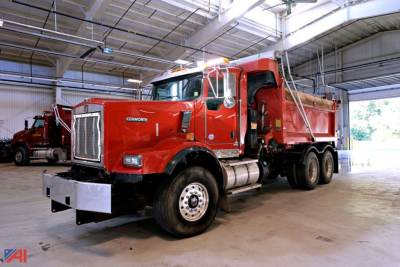 Kenworth T8 Series dump truck in a warehouse showing red cab and dump bed with front bumper and dual rear axles.