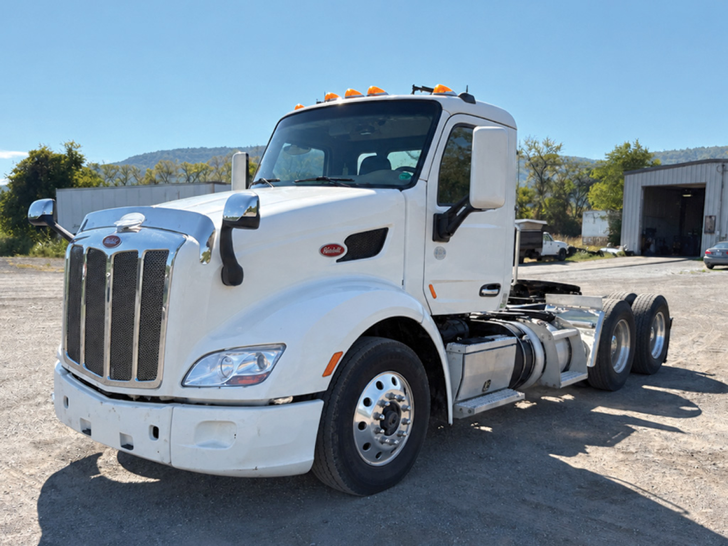 Peterbilt 579 conventional daycab truck in white viewed from front-left with dual rear axles and sleeper cab, cab-mounted mirrors, and orange marker lights.