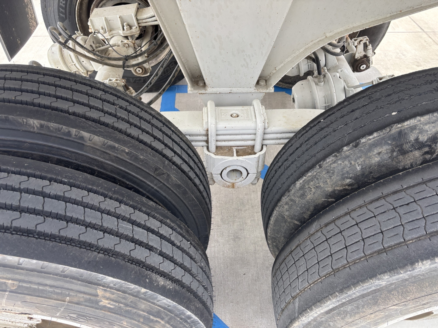 Dual rear trailer wheels and suspension showing chassis beam and tire treads under a dump trailer.