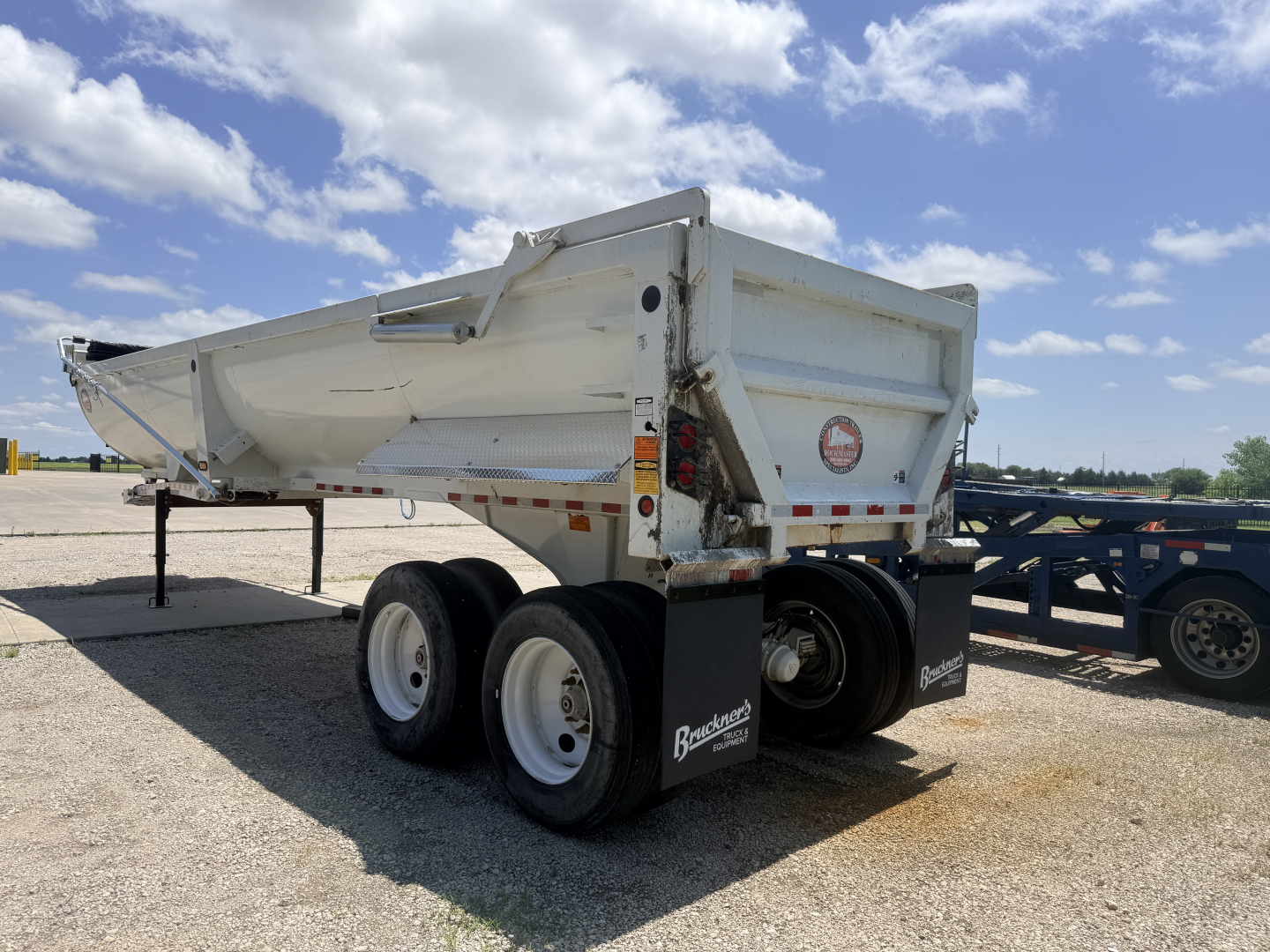 Dump trailer showing dual rear axles with white hopper, BLAINCORP Branded mudflaps and tires; side reflection and VIN plate visible.