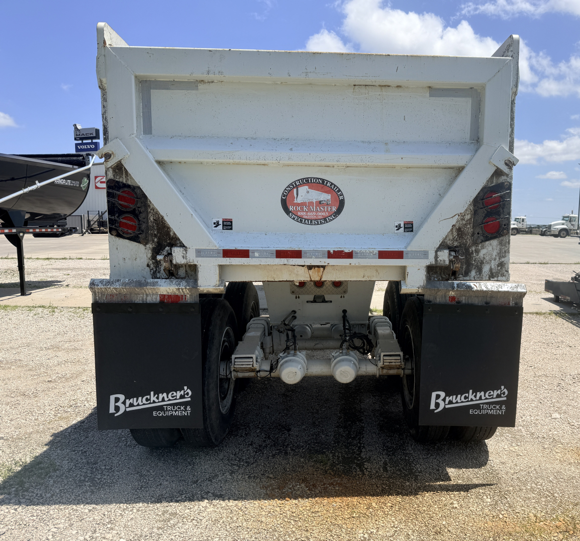 Rear view of a white dump trailer with mud flaps showing Bruckner's Truck & Equipment logo, dual axles, taillights, and a circular Rust-Master badge on the tailgate.