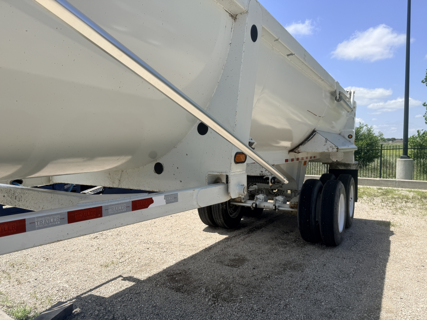Dump trailer side and rear wheel area with white hopper and dual tires under trailer bed, VIN and stock not visible on the image.