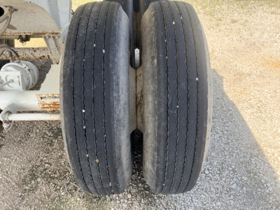 Dual rear trailer tires on a dump trailer axle showing tread wear and metal hub, part of chassis with suspension components visible.