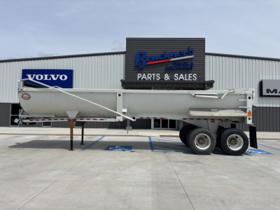 Dump trailer with long white body and dual rear axles parked in front of Braackner truck equipment building showing Volvo sign in background.