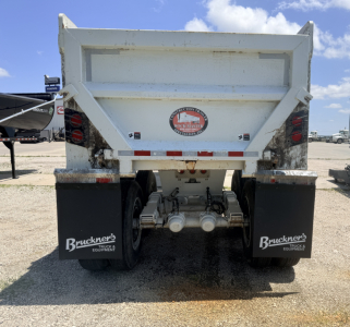 Rear view of a white dump trailer with mud flaps showing Bruckner's Truck & Equipment logo, dual axles, taillights, and a circular Rust-Master badge on the tailgate.