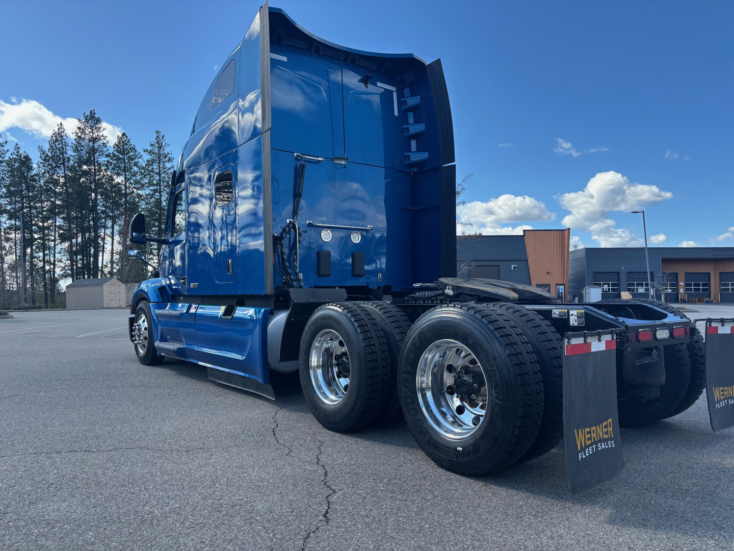 Peterbilt 579 tractor rear quarter view showing dual rear axles with polished chrome wheels, blue sleeper cab, and trailer hitch in a parking lot.