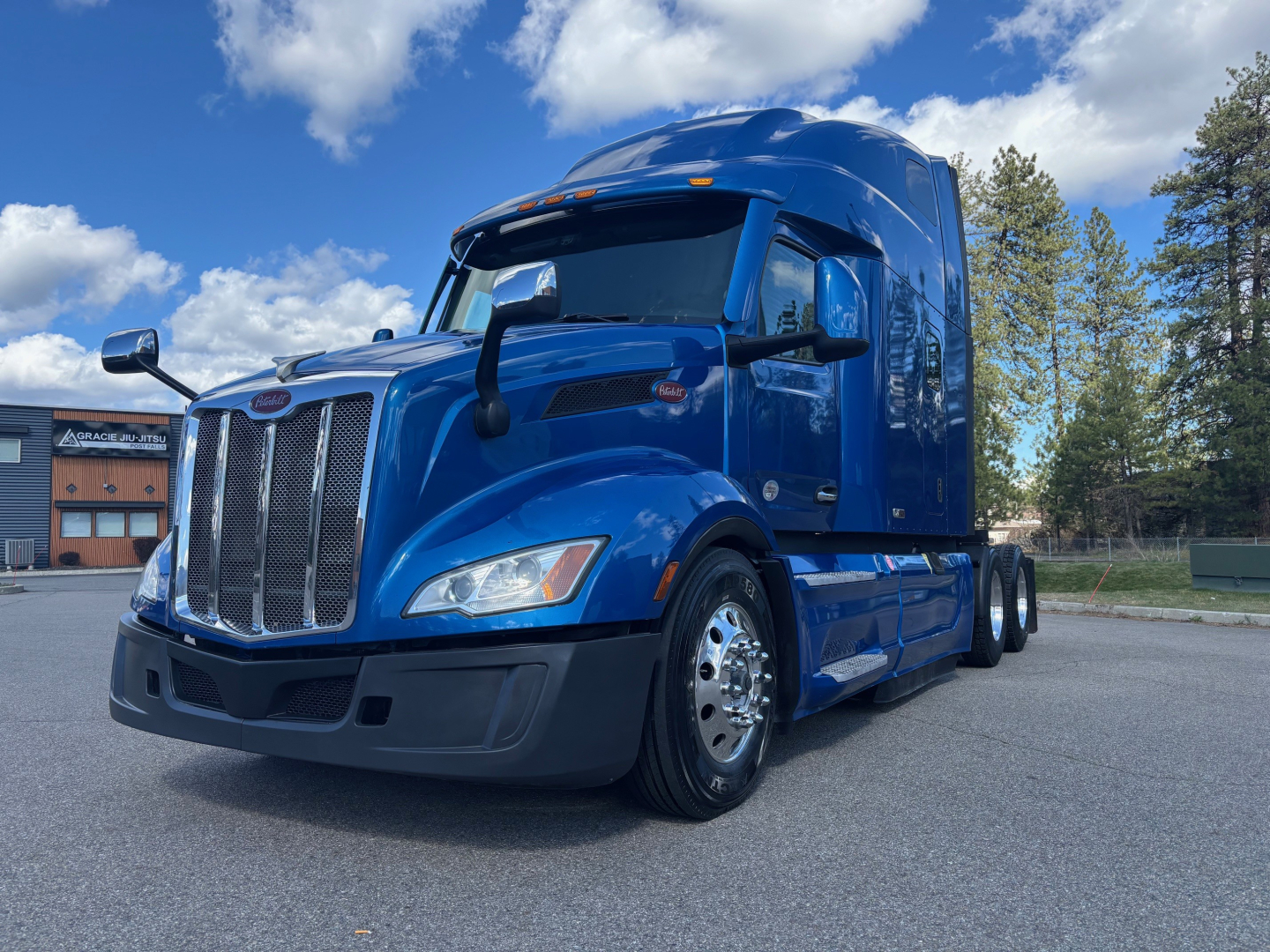 Peterbilt 579 conventional sleeper tractor in blue, front-left view, chrome grille, dual rear axles, daytime running lights.