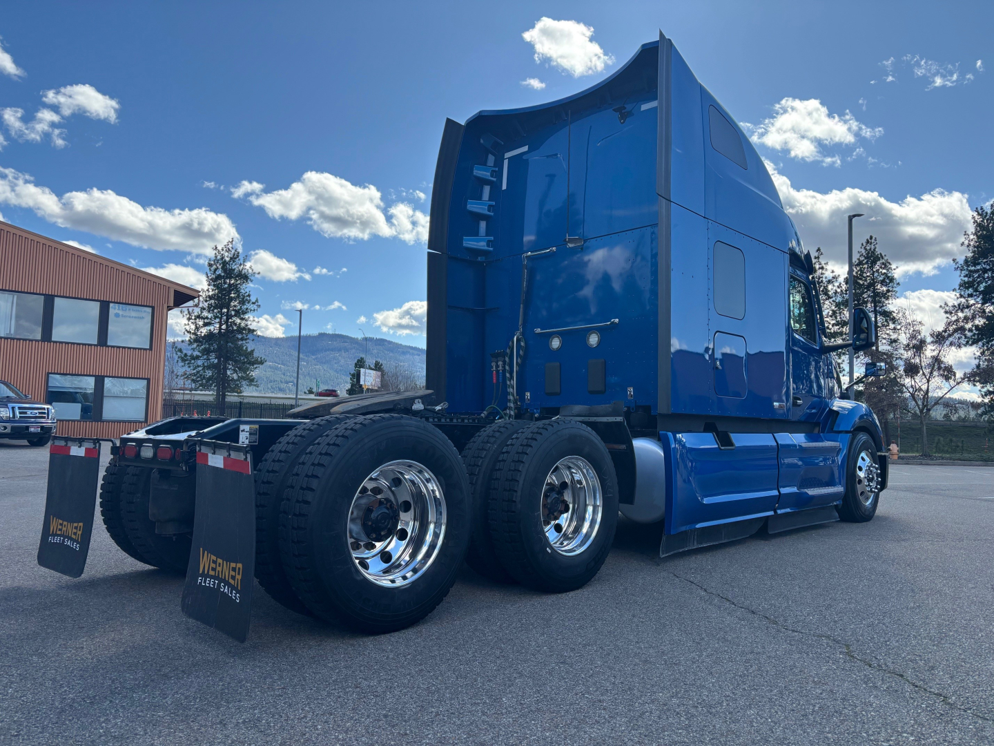 Peterbilt 579 sleeper tractor in blue, side and rear view showing dual rear axles, polished chrome wheels, and HD fuel tanks.