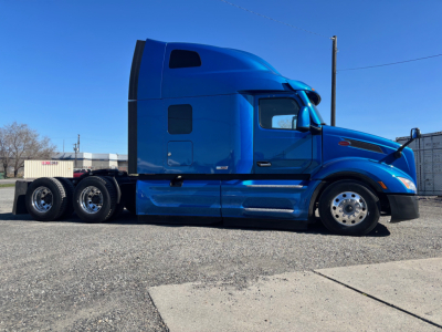 Blue Peterbilt 579 tractor-trailer truck side view with sleeper cab, dual rear axles, and chrome wheels.
