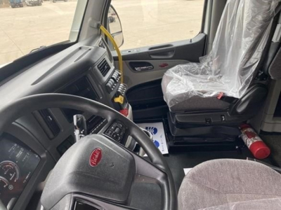 Peterbilt 579 cab interior showing steering wheel, dashboard, driver seat with plastic cover, left door, and gear shifter.
