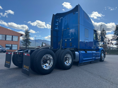 Peterbilt 579 sleeper tractor in blue, side and rear view showing dual rear axles, polished chrome wheels, and HD fuel tanks.