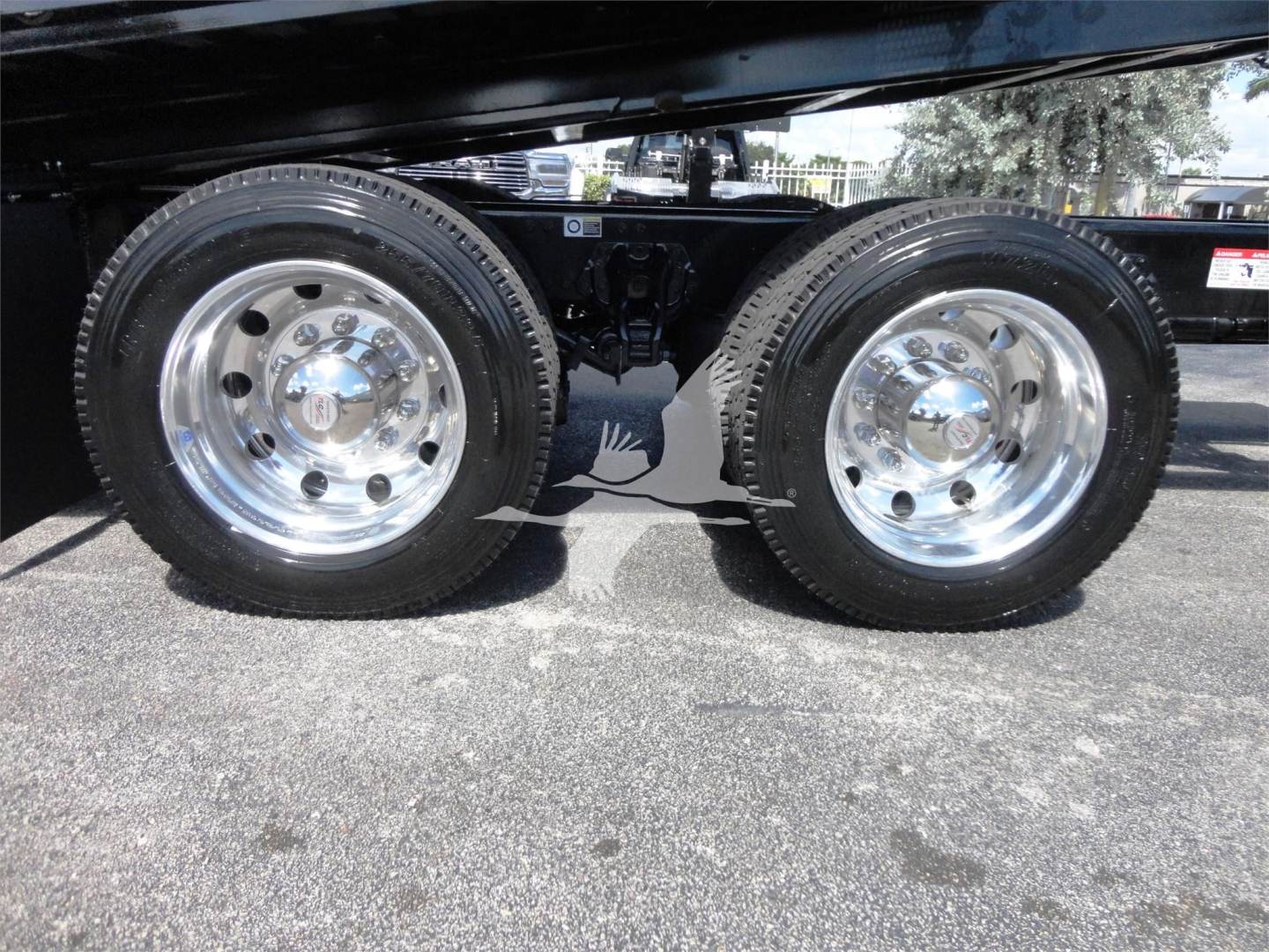 Two rear wheels of a Kenworth W900 chassis with polished rims, dual rear axles visible, undercarriage and suspension components in view.