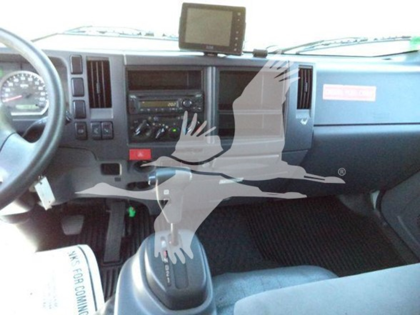 Isuzu NPR dashboard view showing steering wheel, center console, gear selector, and a mounted screen.