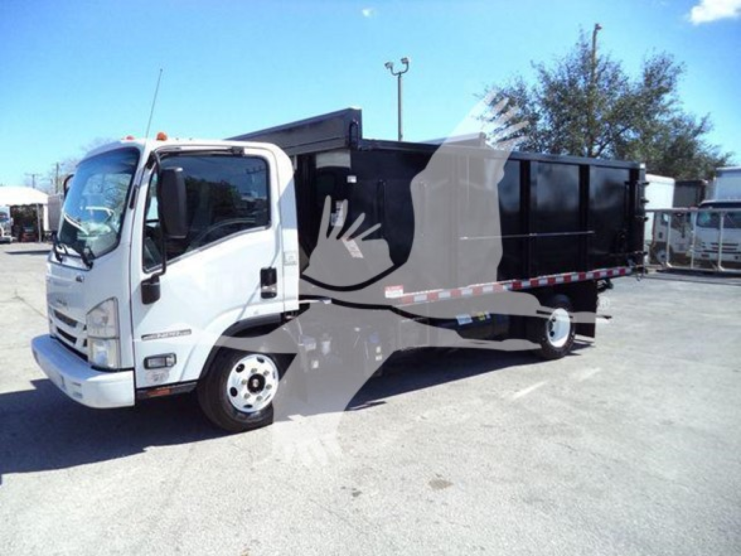 Isuzu NPR dump truck in service showing cab and cargo bed with white cab and black dump body.
