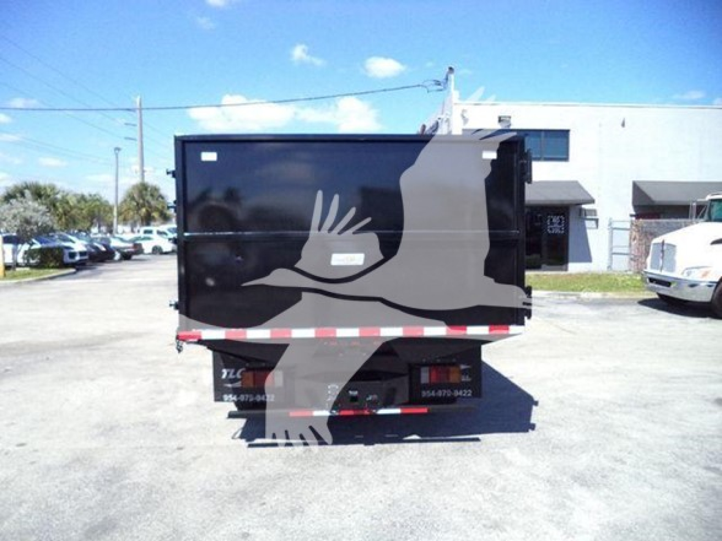 Truck dump trailer at a dealership lot showing rear view with black dump bed and reflection of other vehicles.