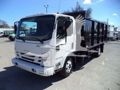 Isuzu NPR dump truck side view showing cab and dump body, white cab, black dump bed, front grille with Isuzu emblem, daytime outdoor lot.