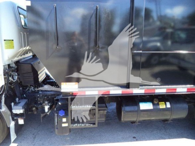 Isuzu NPR dump truck side showing engine bay and fuel/tank area with side graphics and warning labels.