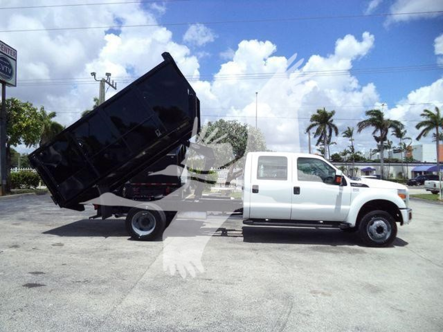 Ford F-550 dump truck with black dump bed raised, white cab, side view showing dual rear wheels and hydraulic lift.
