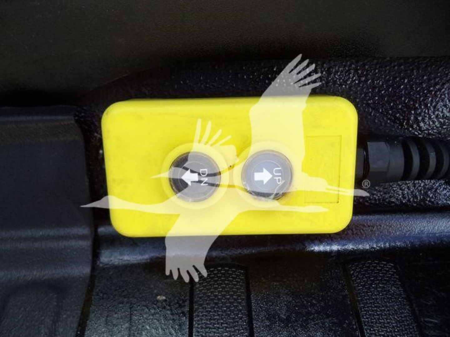 Yellow two-button control box with up/down arrows mounted in a vehicle floor area.