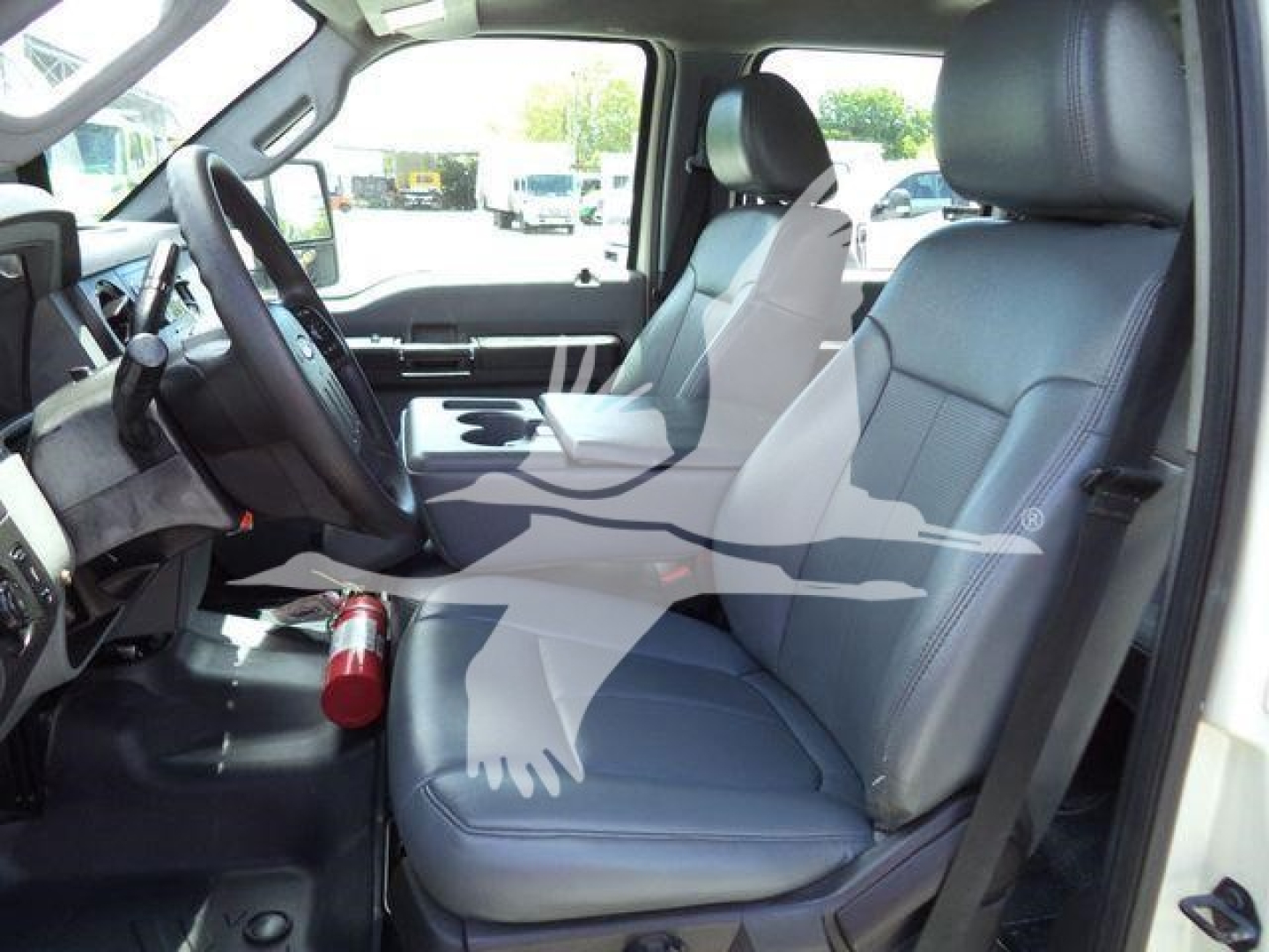 Ford F-550 interior with front seats and steering wheel; center console; visible dashboard; cup holder; seat belts; light gray upholstery.