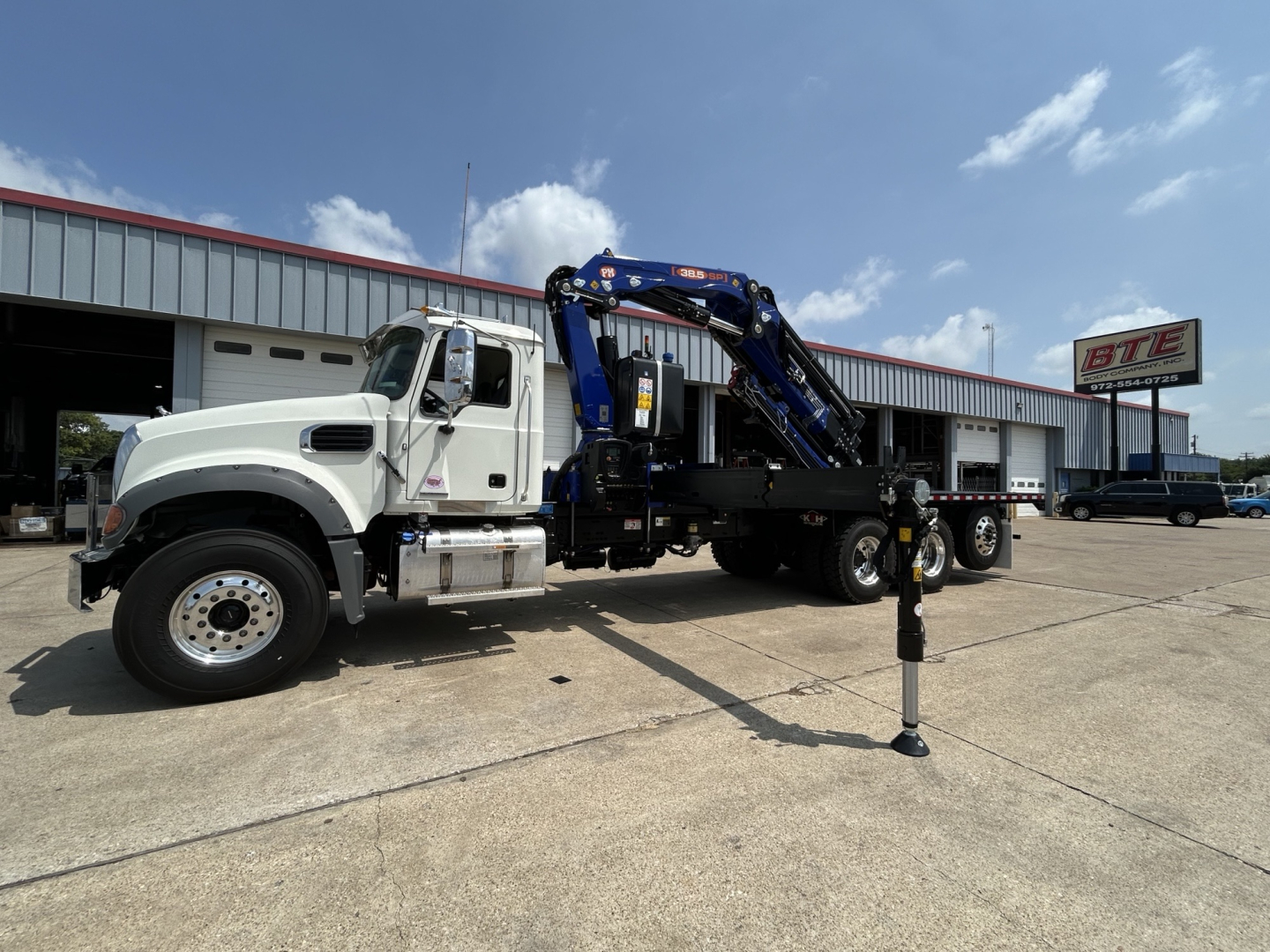 Grayscale-free Mack GR64F crane truck in a parking lot showing jib crane and stabilizer out, white cab with blue crane, stock number and VIN not visible on text