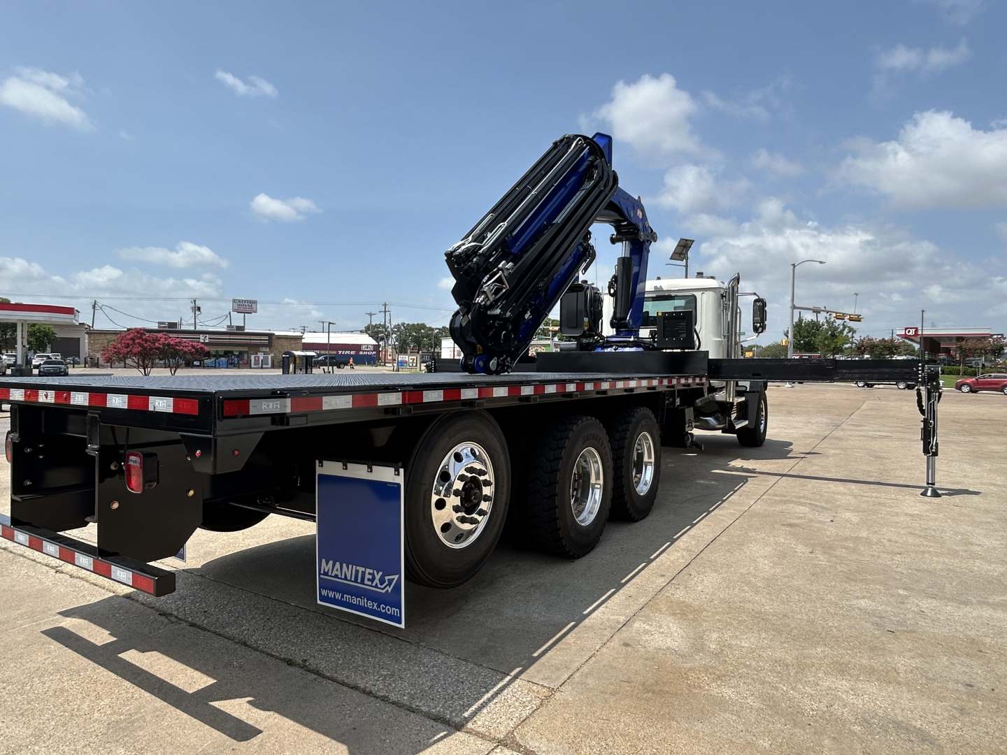 2027 Mack GR64F crane truck under extended boom on trailer with outriggers, side view showing crane components and tires.
