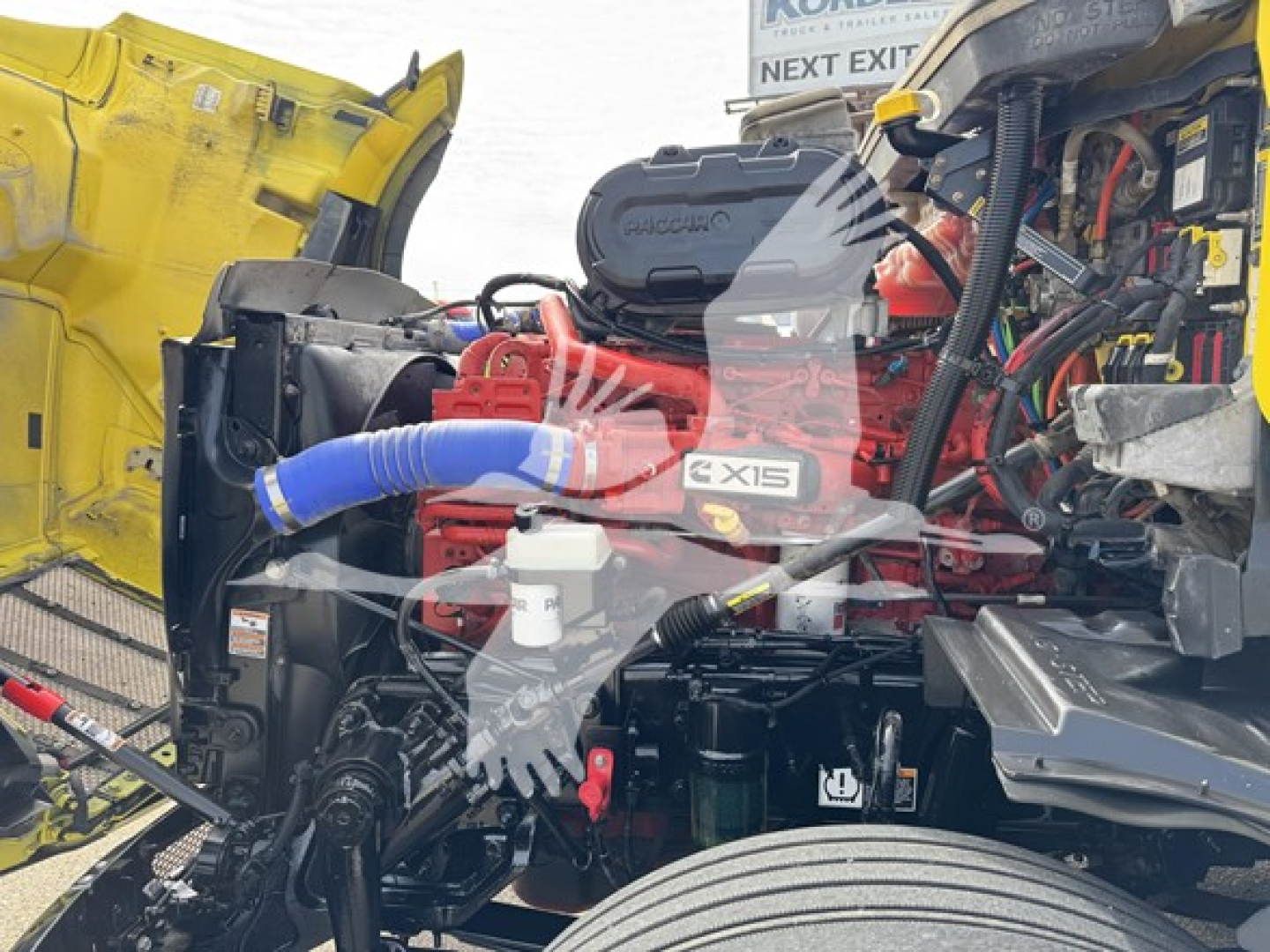 Truck engine bay of a 2024 Peterbilt 579 showing Cummins X15 engine with blue coolant hose and surrounding components.