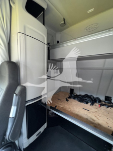 Peterbilt 579 cab interior showing sleeper bunk and overhead storage with visible plywood floor and scattered tools.