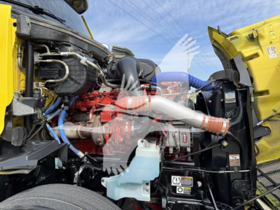 Peterbilt 579 engine bay with exposed red turbo-diesel engine, blue hoses, coolant reservoir, and yellow body panels.