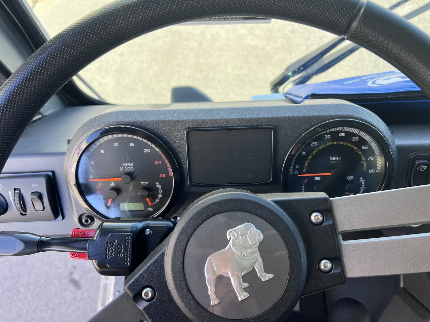 Truck dashboard and steering wheel showing tachometer and speedometer gauges with center display; visible Bulldog logo on steering wheel hub.