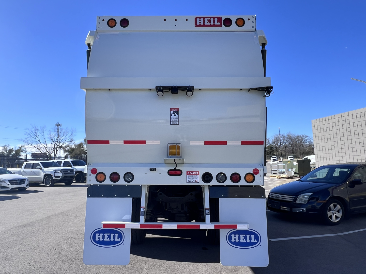 Rear view of a white Mack TE64 garbage truck showing HEIL branding, taillights, and reflective stripes; VIN and stock info not visible. 