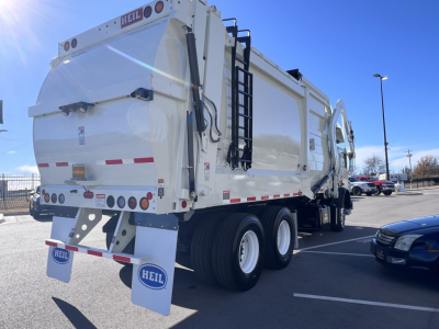 Rear view of a white HEIL garbage truck body mounted on a Mack TE64 or similar chassis, with dual rear wheels, ladders, and tailgate plates visible.