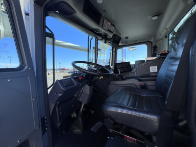 Truck cabin interior showing steering wheel, dashboard, and driver's seat of a new Mack TE64 with visible control panels and screens.